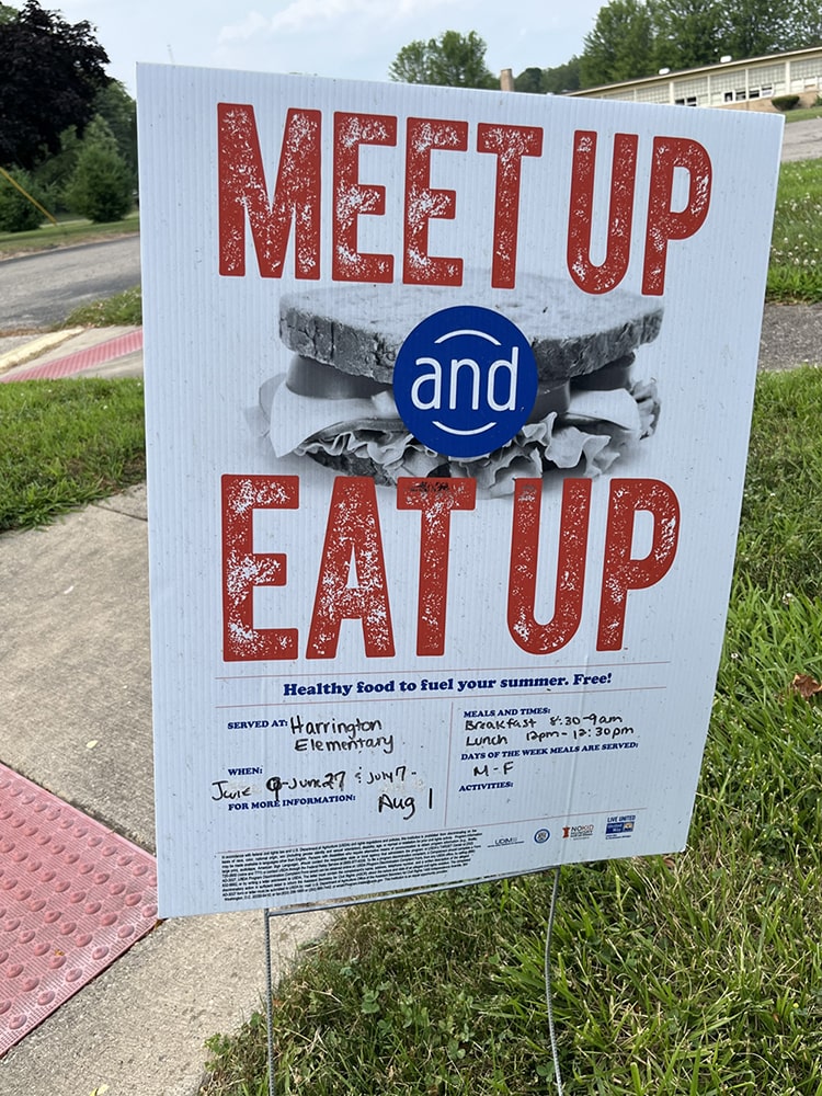 A sidewalk sign outside Harrington Elementary School promotes the Meet Up and Eat Up summer meals program. Free breakfast and lunch are available on weekdays for youth 18 and under at several locations around Albion.