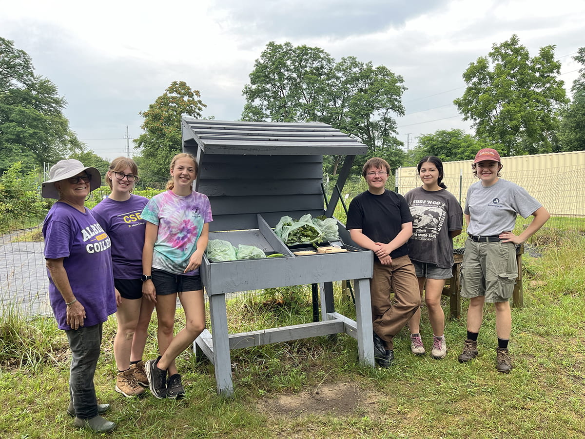 Garden helpers gather around the Albion Community Gardens’ produce stand, where fresh-picked greens are set out for the public each Monday, Wednesday, and Friday morning. The food is free, and updates are shared on social media. From the left, Trisha Franzen, Emma Kastl, Ana Metz, Maddie Crosby, Dahalia Aguilar and Bonnie Lord.