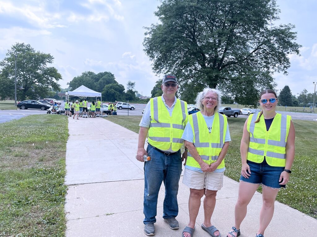 Terry and Dana Anderla, longtime volunteers, stand with Amanda Cheladyn, manager of the Community Table of Albion at the new distribution location at the high school. Volunteers in high-visibility vests help guide traffic and distribute food to residents who come to get the food.